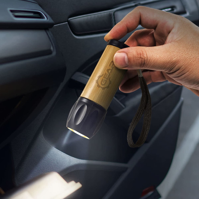 A hand holds a bamboo torch with a black end, illuminated, inside a vehicle. It features a branding logo.