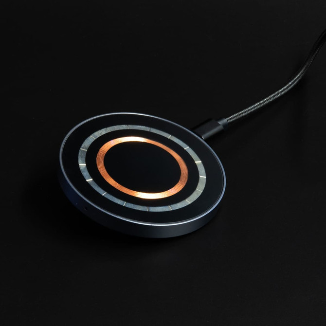 A round, black and silver wireless charger with a copper centre and a textured cable connected.