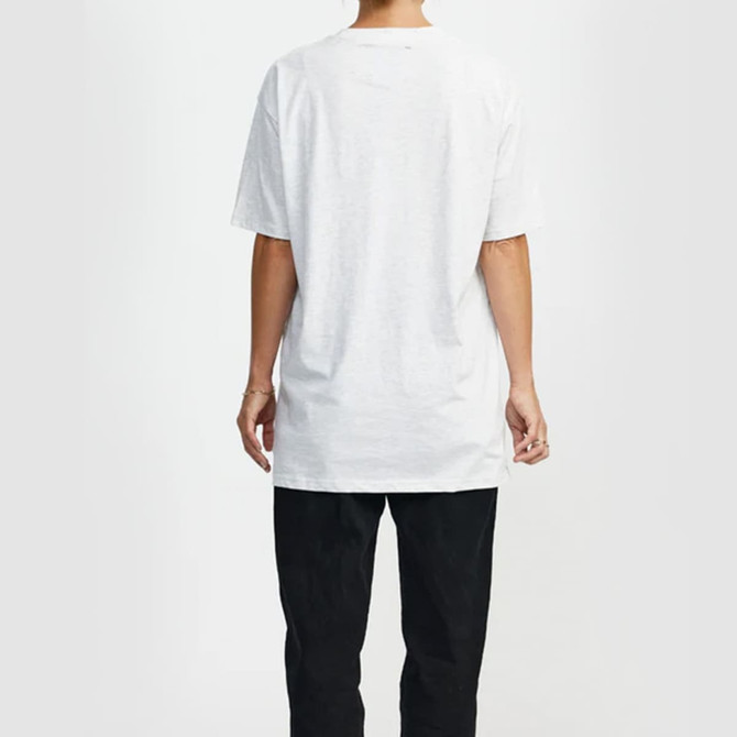 A white t-shirt with short sleeves is displayed on a person from the back, paired with black trousers. The shirt features a logo.