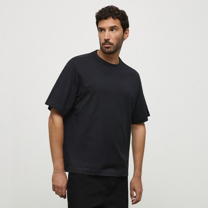 A black essential tee displayed on a model, featuring a relaxed fit and short sleeves. It has a logo on the garment.