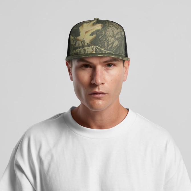 A camo trucker cap in shades of green and brown, worn by a model in a white t-shirt. It features a logo on the front.