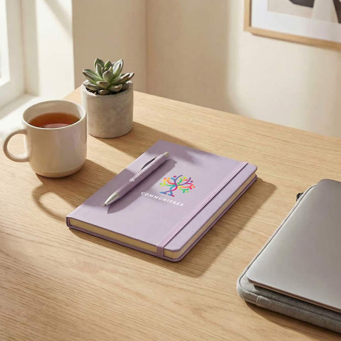 A lavender notebook with a pen rests on a wooden desk, alongside a mug and a succulent plant.