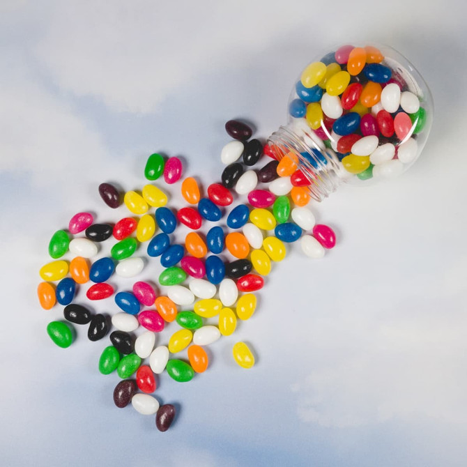 A container spilling assorted colour mini jelly beans in vibrant hues of pink, yellow, green, blue, and more.