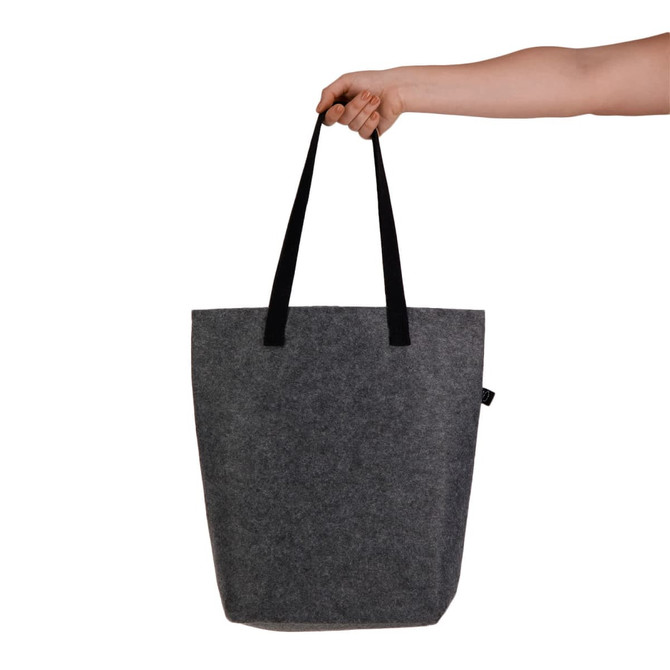 A hand holds a grey felt tote bag with black straps. The bag features a branding logo.