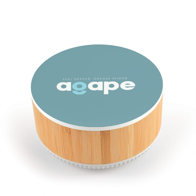 A round speaker and wireless charger with a bamboo base and a teal top featuring a logo.