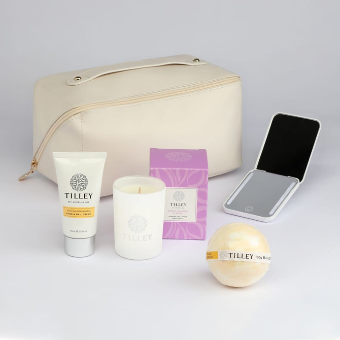 A cream toiletry bag with a scented candle, hand cream, a bath bomb, and a mirror. Featuring a logo on the bag.