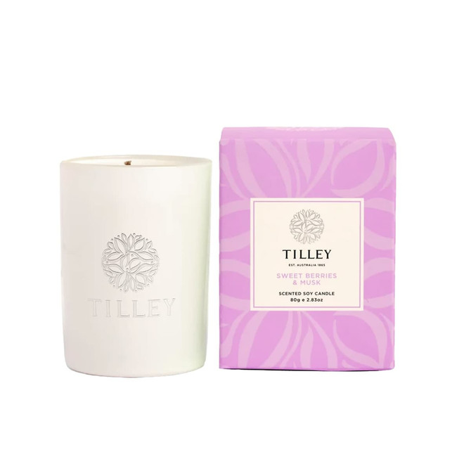 A white scented soy candle is accompanied by a purple box, labelled "Sweet Berries & Musk", featuring a logo.