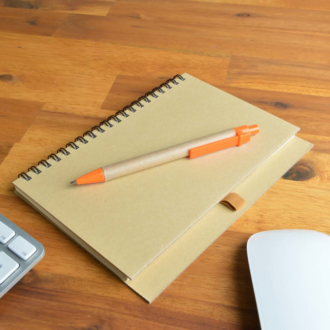 A brown spiral-bound notebook with a kraft paper cover and an orange Matador pen resting on top, placed on a wooden surface.