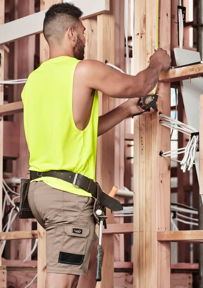 A man wearing khaki cargo shorts and a bright yellow sleeveless top, working with tools on a construction site.