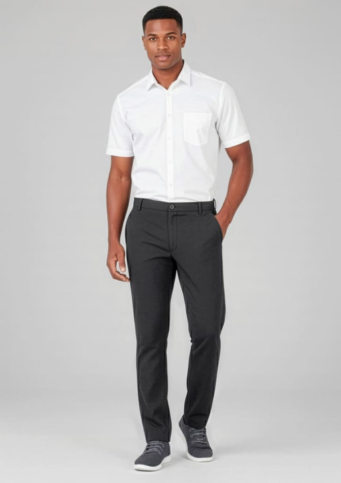 A man wearing black flat front slacks paired with a white short-sleeve shirt and grey sneakers. There is a logo on the slacks.
