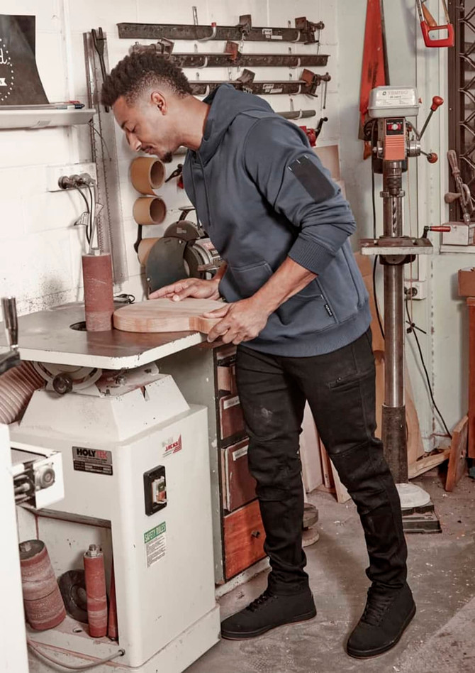 A unisex multi-pocket hoodie in navy, worn by a person working with wood in a workshop setting, alongside various tools.
