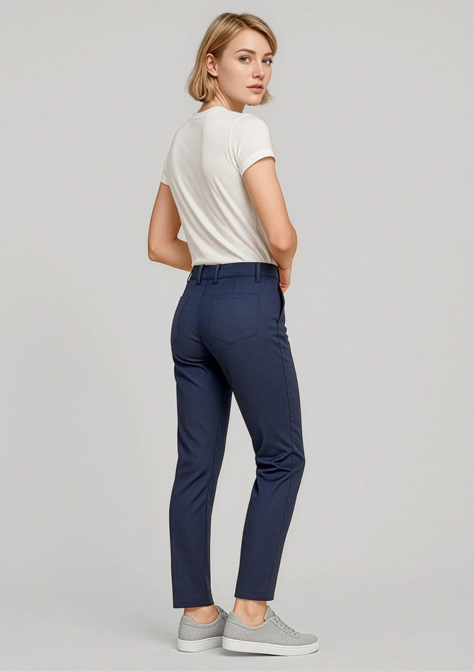 A woman stands wearing navy slim leg stretch chino pants and a white top, paired with grey sneakers.