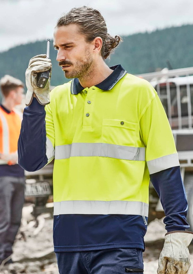 A man wears a bright yellow and navy long sleeve polo with reflective tape, holding a walkie-talkie. It has a logo.