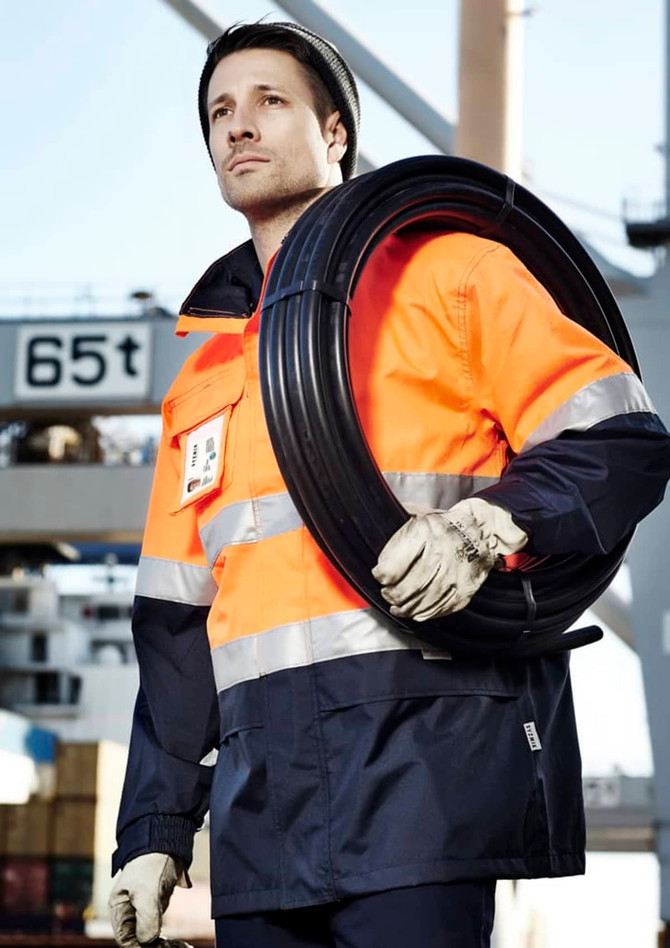 A man wearing an orange and navy waterproof jacket holds a coil of wire, showcasing a high-visibility workwear design.