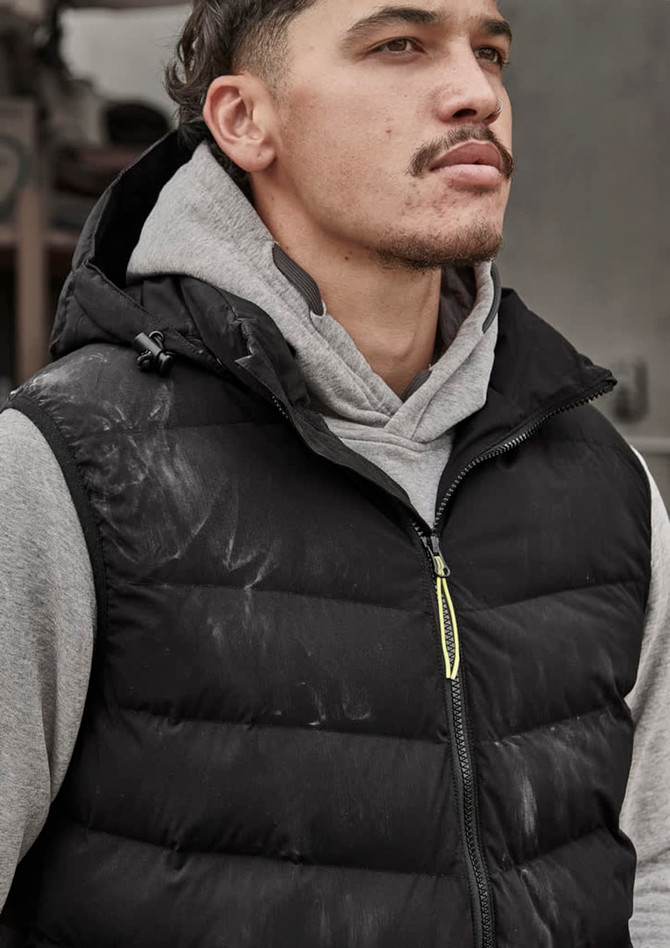 A unisex black hooded puffer vest is worn over a grey hoodie. The vest features a logo and a zip closure.