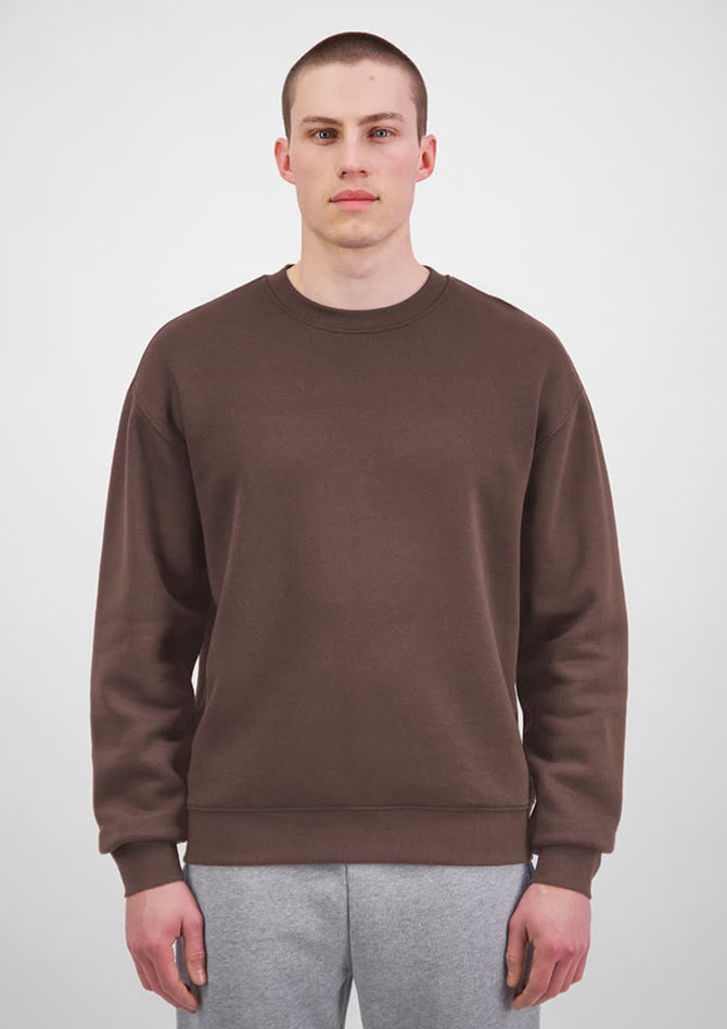 A brown crew sweatshirt for men, featuring a simple design and relaxed fit, shown on a model with grey pants.