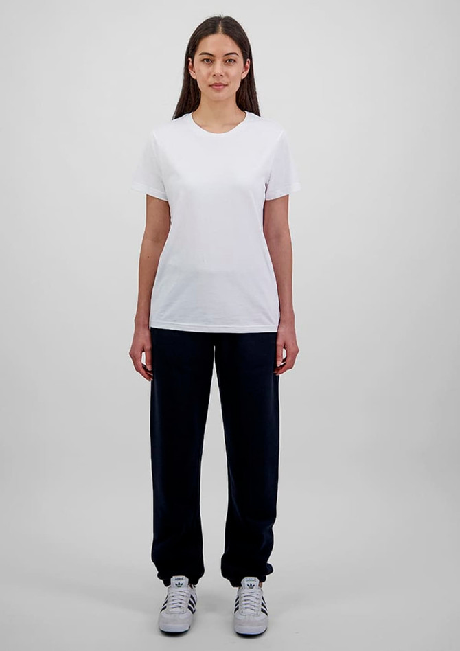 A woman stands wearing a white t-shirt and navy blue track pants, showcasing a simple, casual outfit.