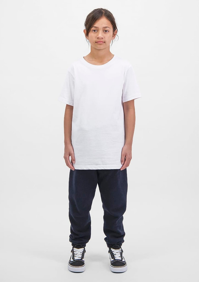 A child wears a white t-shirt and navy track pants, standing against a plain white background. The outfit features a logo.