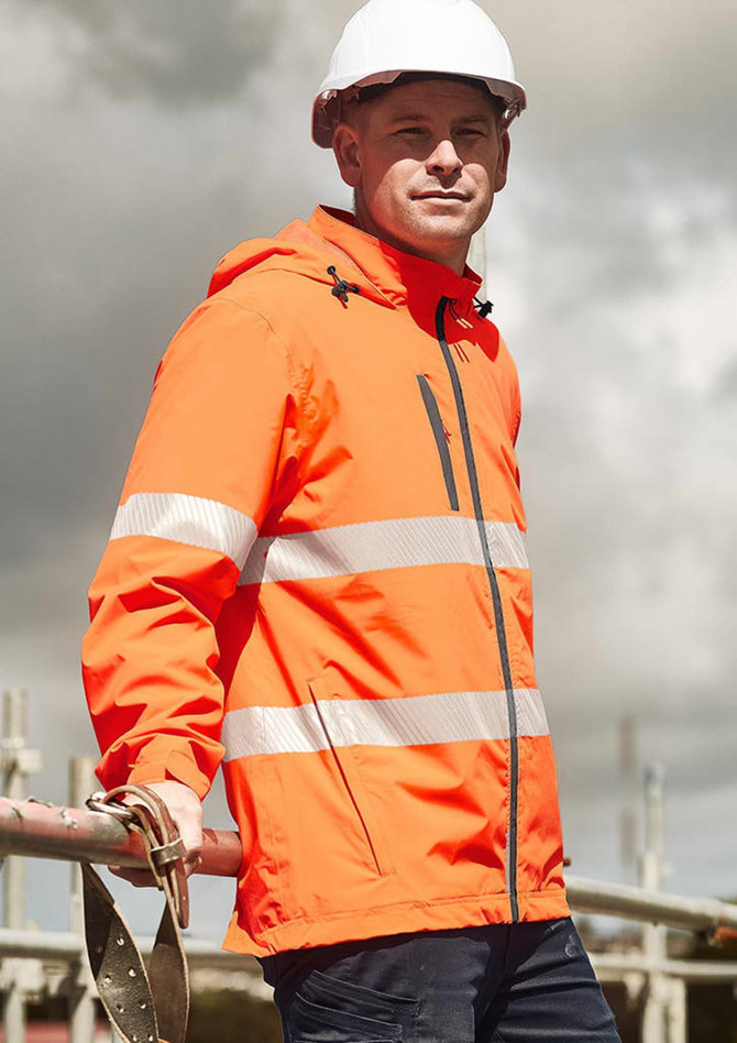 A bright orange packable rain jacket with reflective stripes, worn by a model on a construction site.