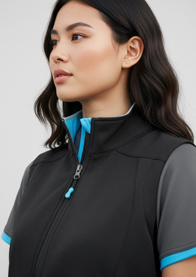 A woman models a black vest with blue accents, featuring a stand-up collar and a zipper. The vest has a logo.