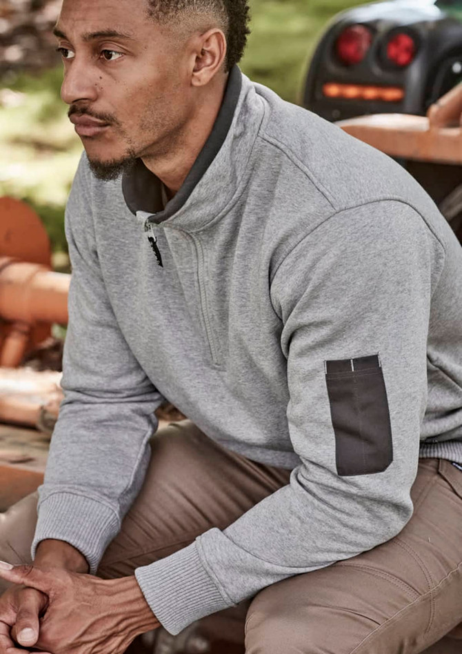 A man wearing a grey unisex 1/4 zip brushed fleece pullover with a logo on the sleeve, seated outdoors.
