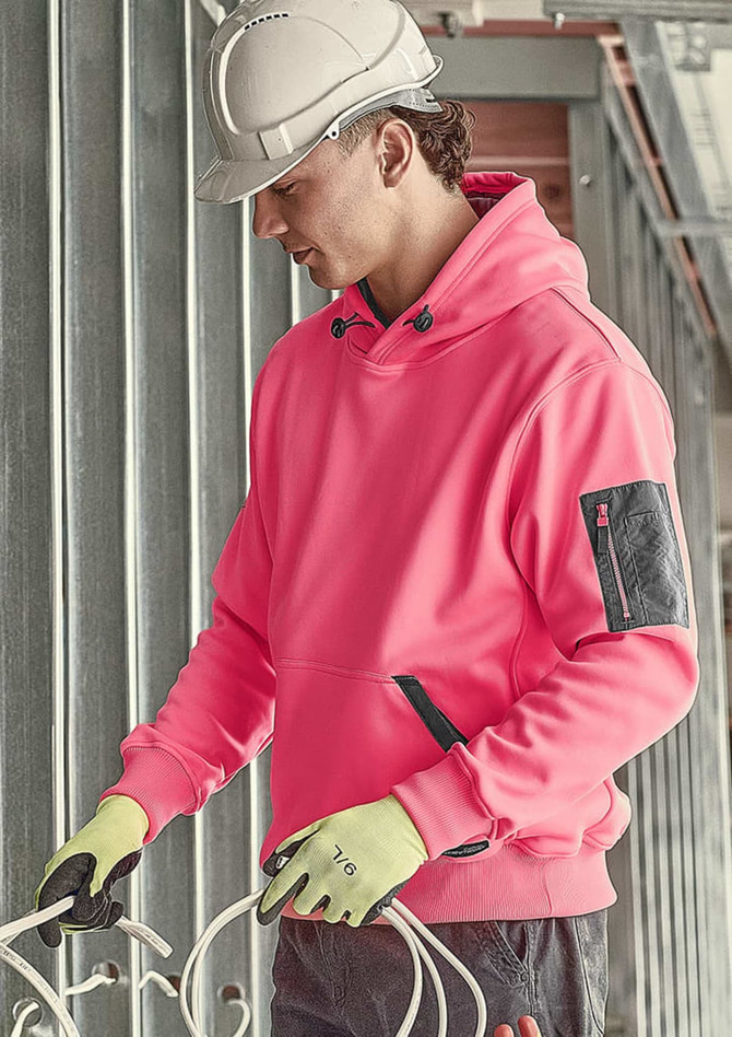 A pink unisex water-resistant hoodie with a pocket, worn by a person in a hard hat and gloves, in a construction setting.