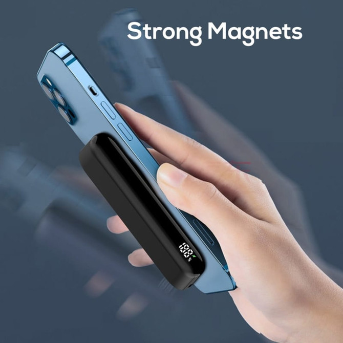 A black magnetic power bank with a digital display, being held next to a blue phone.