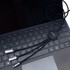 A black charging cable with multiple connectors lies on a laptop keyboard. The cable features a circular connector with branding.