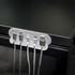 A cable organiser in grey holds multiple charging cables against a black surface. It features a fabric-like texture and a sleek design.