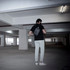 A man in a black shirt and light trousers is carrying a grey anti-theft sling bag in a parking garage.