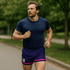 A man runs in purple and pink shorts, paired with a navy blue T-shirt, amid a green park setting.