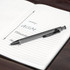 A metal pen with a sleek grey finish rests on a lined notebook, which features handwritten notes.