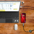 A LED charging cable in black, connected to a smartphone and a laptop, on a wooden table with accessories.
