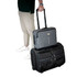 A grey laptop bag with wheels is stacked on a black wheeled suitcase, held by a person in casual attire.
