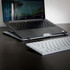 A grey laptop stand supports a laptop on a dark wooden desk, with a white keyboard nearby.