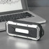 A rugged black and silver waterproof Bluetooth speaker placed beside a laptop on a metallic surface.