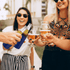 A drink bottle holder in navy blue, surrounded by glasses of beer and cheers among friends in an outdoor setting.