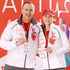 Two individuals wearing white Egmont Packable Jackets with a logo, posing with medals and a red hat.