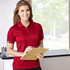A woman wearing a red short sleeve polo shirt with a logo, holding a clipboard and smiling.