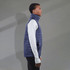 A navy puffer vest with a high collar, worn over a long-sleeve white top, featuring a logo on the chest.