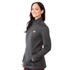 A woman wearing a grey softshell jacket with a logo, featuring a zip-up front and side pockets.