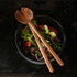 A set of wooden salad servers rests on a bowl filled with mixed greens and vegetables.