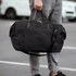A black duffle bag is being held by a person, featuring dual handles and a shoulder strap.