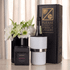 A wine bottle in a white cooler, surrounded by a black box and a flower arrangement in a black vase.