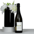 A sparkling wine bottle with a black label next to a black vase filled with white flowers.
