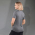 A woman wears a grey polo shirt with short sleeves, featuring a logo on the back. The background is neutral.