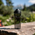 A drink bottle in a sleek, transparent design with a black lid and handle, set against a natural outdoor backdrop.