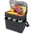 A double compartment cooler bag in charcoal grey, containing snacks, fruit, and drink cans. It has a logo and an unzipped lid.