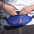 A blue bum bag featuring a floral design, being worn by a person with hands adjusting it.