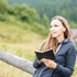A woman holding a black Spectrum Pocket Notebook while sitting outdoors in a natural setting.